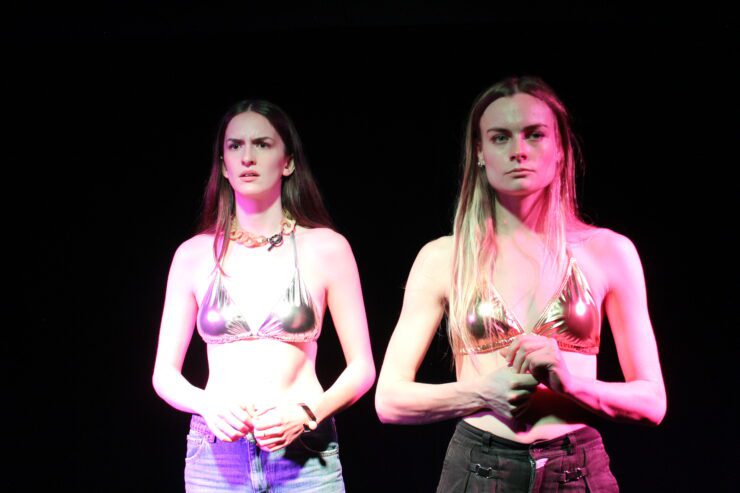 Two girls in gold bikini tops bathed in pinky-purple lights